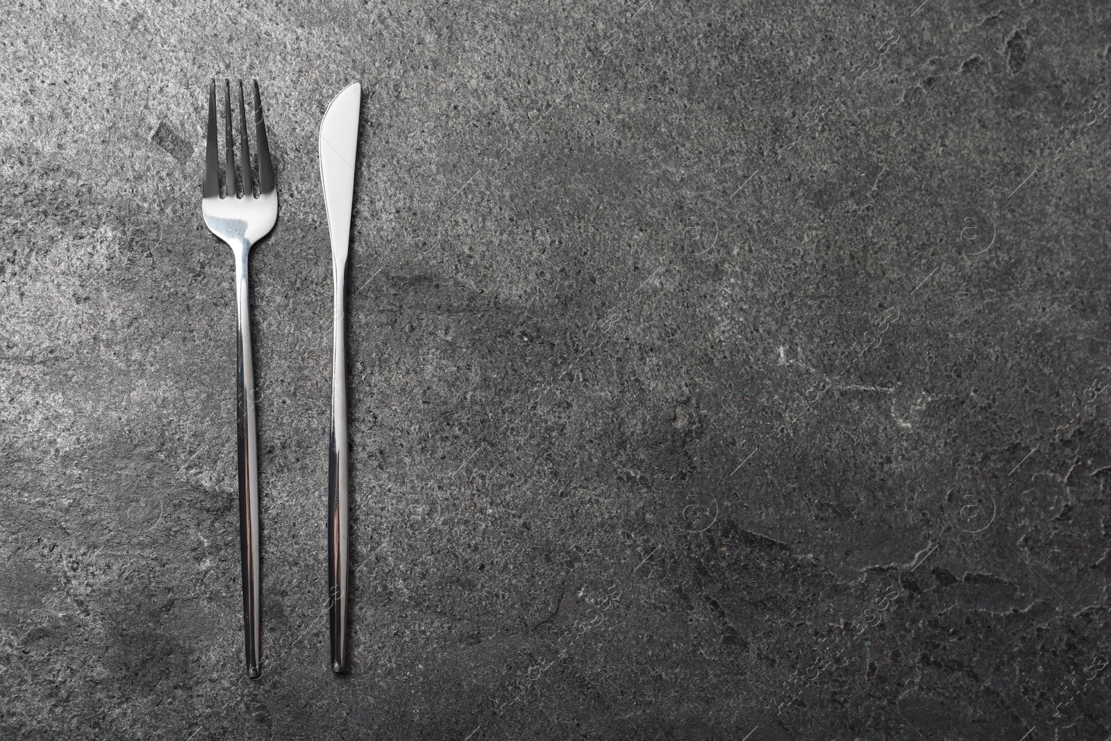 Photo of Stylish silver cutlery on grey table, top view. Space for text