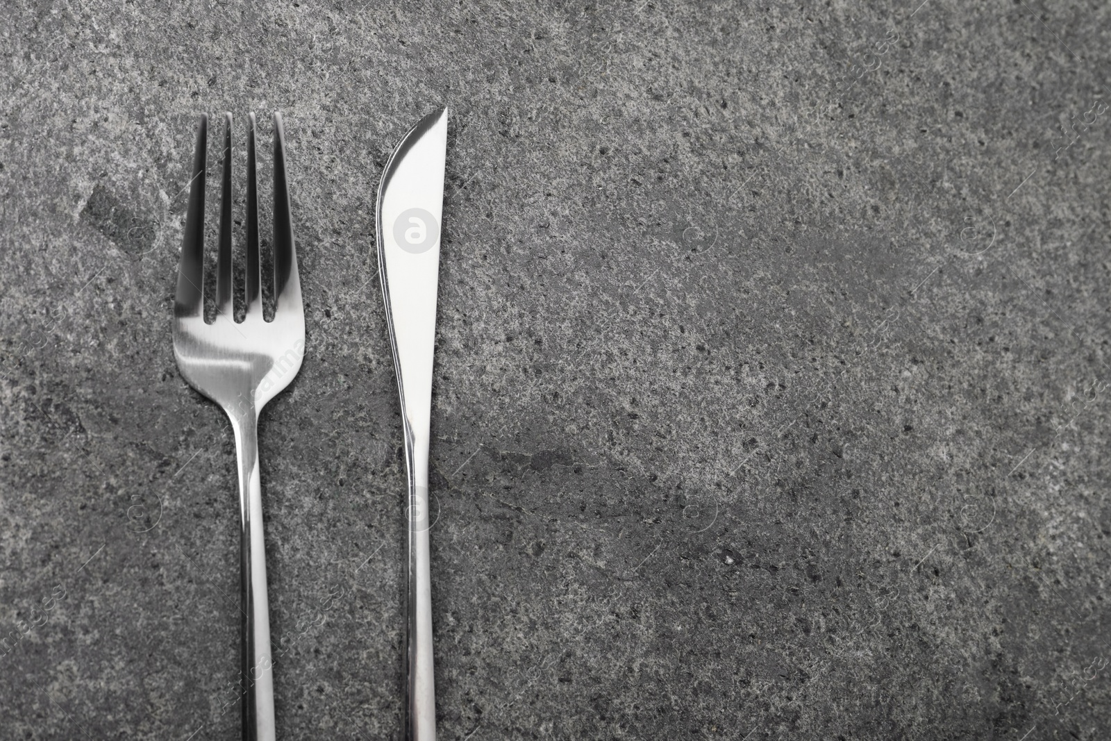 Photo of Stylish silver cutlery on grey table, top view. Space for text