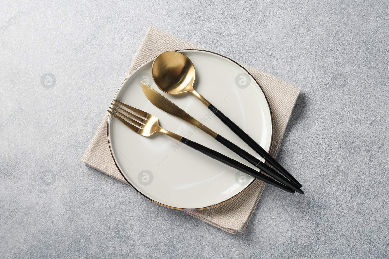 Photo of Stylish golden cutlery, plate and napkin on grey table, top view