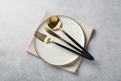 Photo of Stylish golden cutlery, plate and napkin on grey table, top view