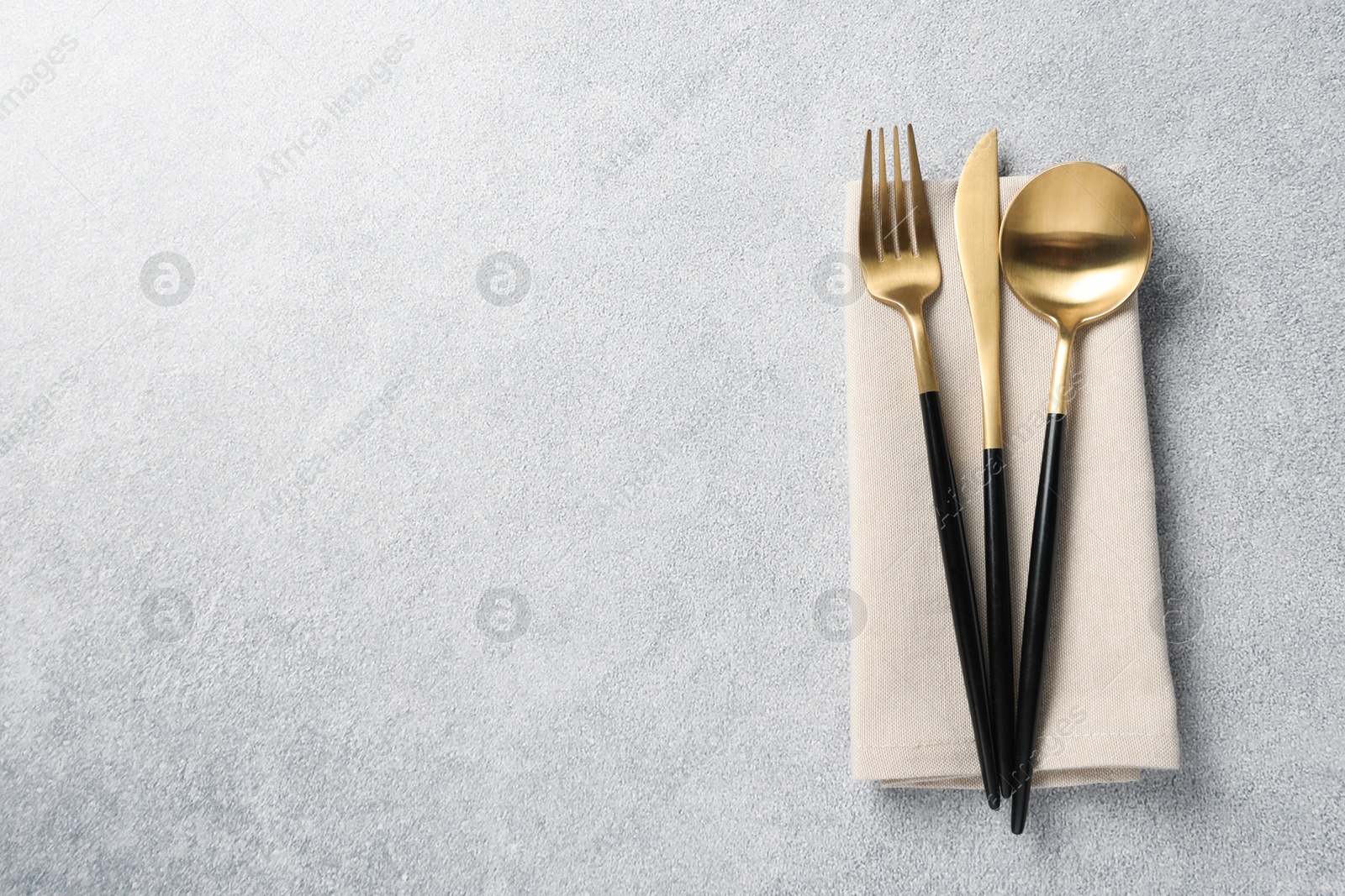 Photo of Stylish golden cutlery and napkin on grey table, top view. Space for text