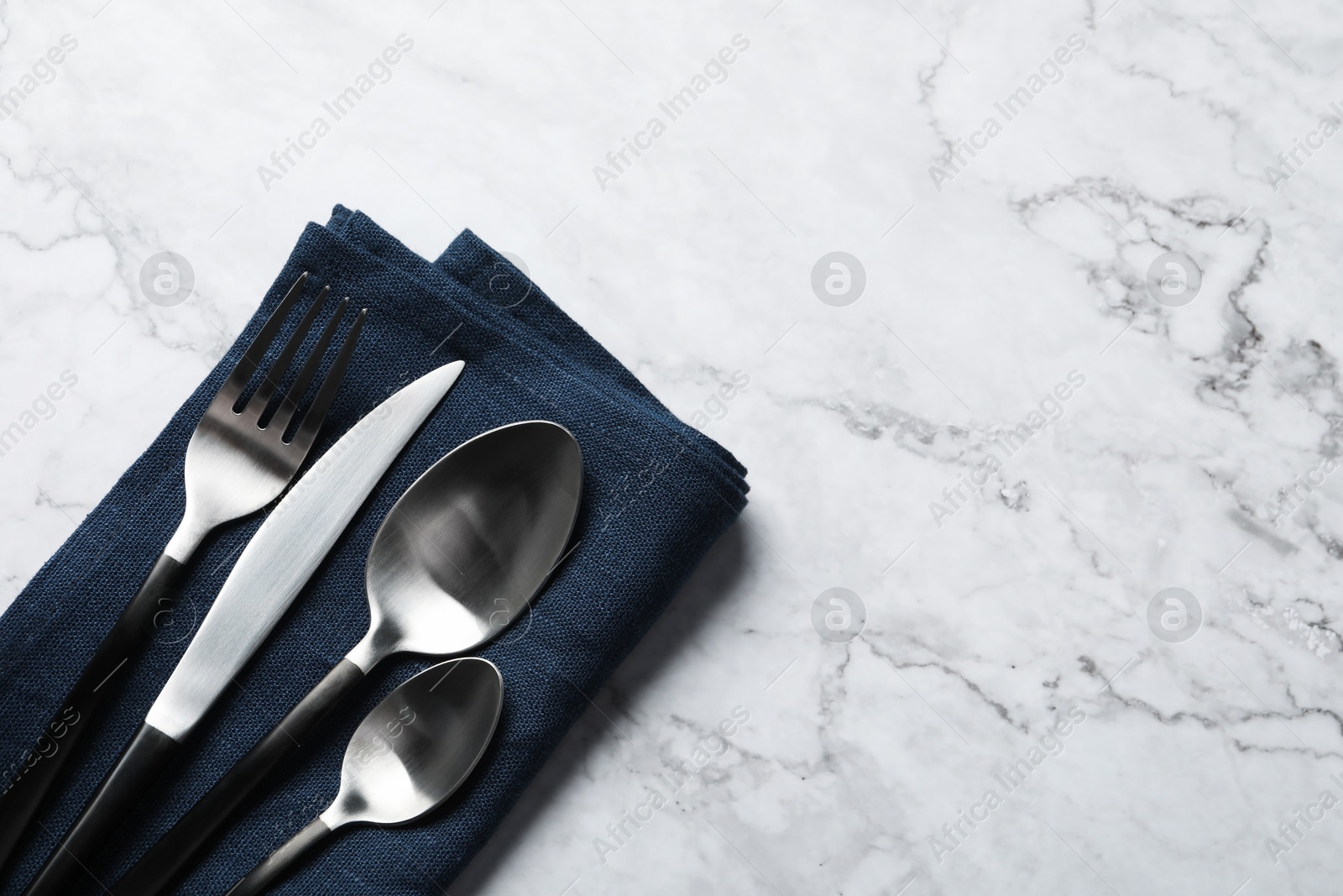 Photo of Stylish cutlery and napkin on white marble table, top view. Space for text