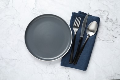 Photo of Stylish cutlery, napkin and plate on white marble table, top view