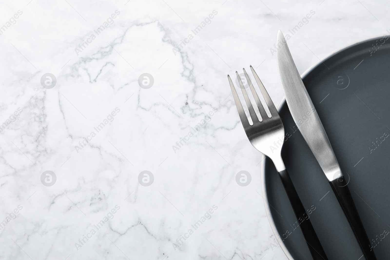 Photo of Stylish cutlery and plate on white marble table, top view. Space for text