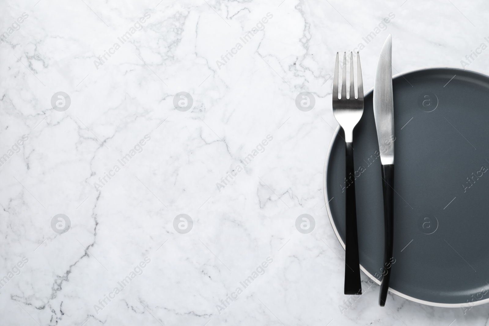 Photo of Stylish cutlery and plate on white marble table, top view. Space for text