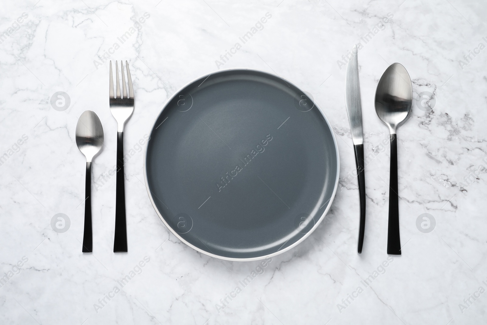 Photo of Stylish cutlery and plate on white marble table, flat lay