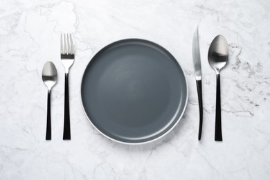 Stylish cutlery and plate on white marble table, flat lay