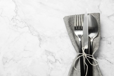 Photo of Stylish cutlery and napkin on white marble table, top view. Space for text