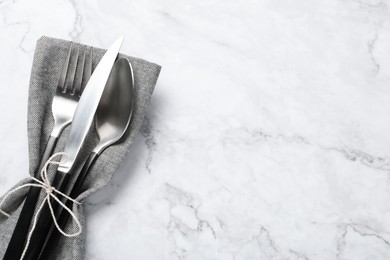 Photo of Stylish cutlery and napkin on white marble table, top view. Space for text