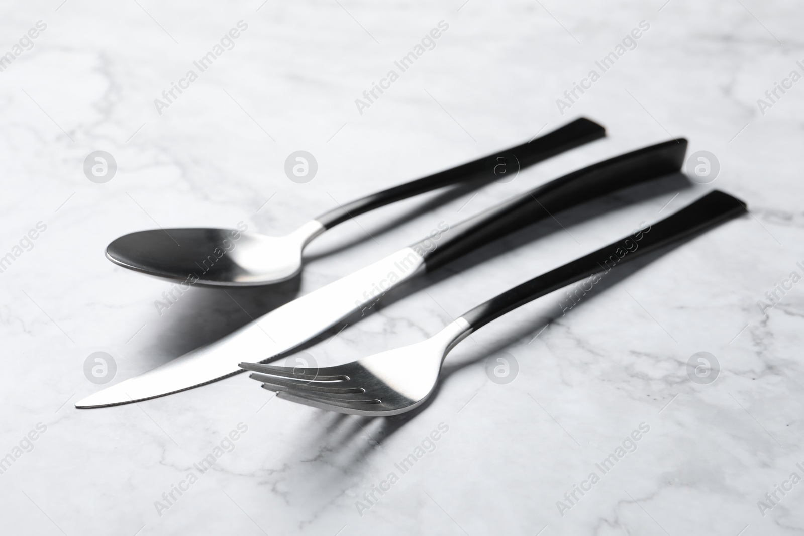 Photo of Stylish cutlery. Fork, spoon and knife on white marble table