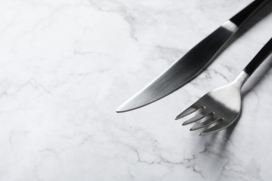 Photo of Stylish cutlery. Fork and knife on white marble table, space for text