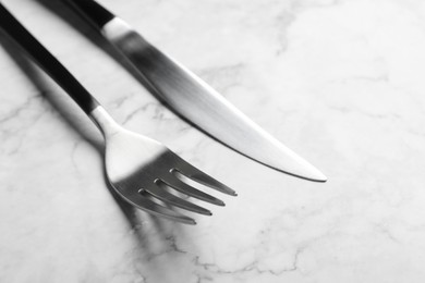 Photo of Stylish cutlery. Fork and knife on white marble table, closeup