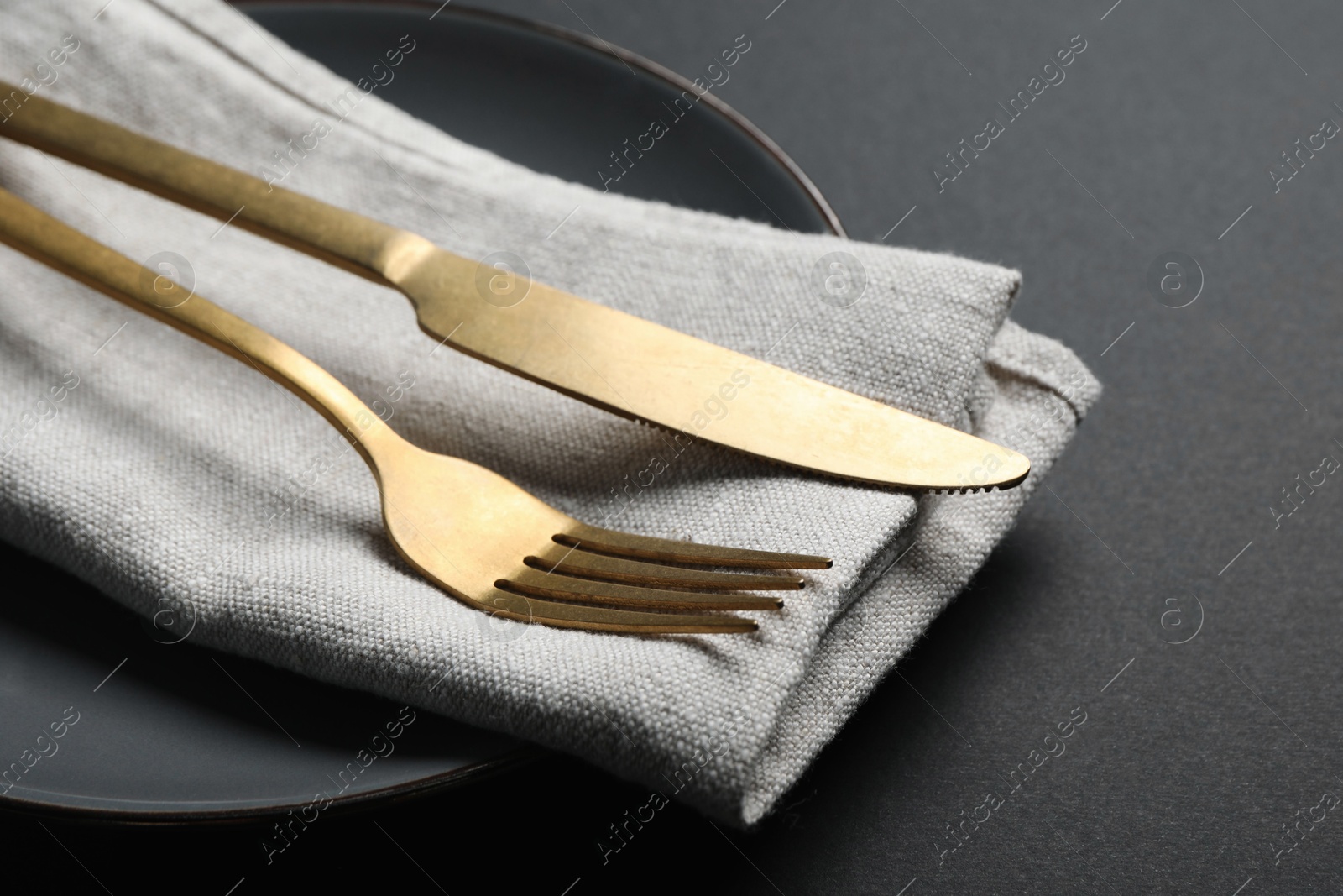 Photo of Elegant golden cutlery, napkin and plate on black background, closeup