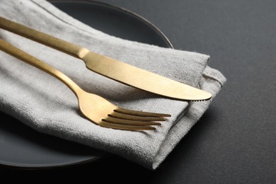 Photo of Elegant golden cutlery, napkin and plate on black background, closeup