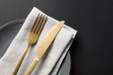 Photo of Elegant golden cutlery, napkin and plate on black background, top view. Space for text