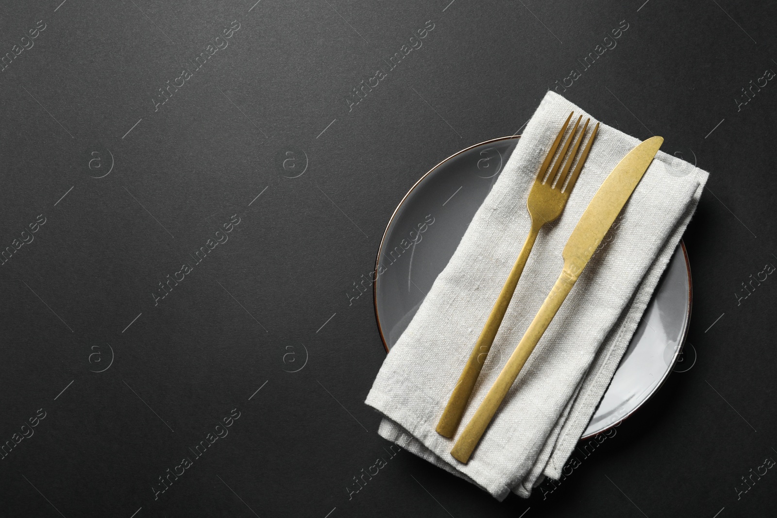 Photo of Elegant golden cutlery, napkin and plate on black background, top view. Space for text