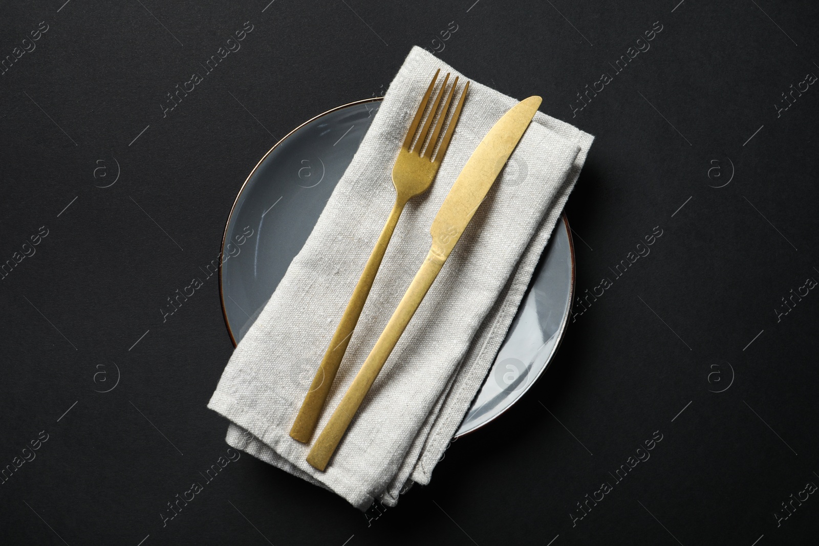 Photo of Elegant golden cutlery, napkin and plate on black background, top view