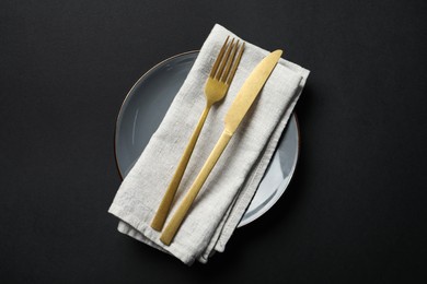 Photo of Elegant golden cutlery, napkin and plate on black background, top view