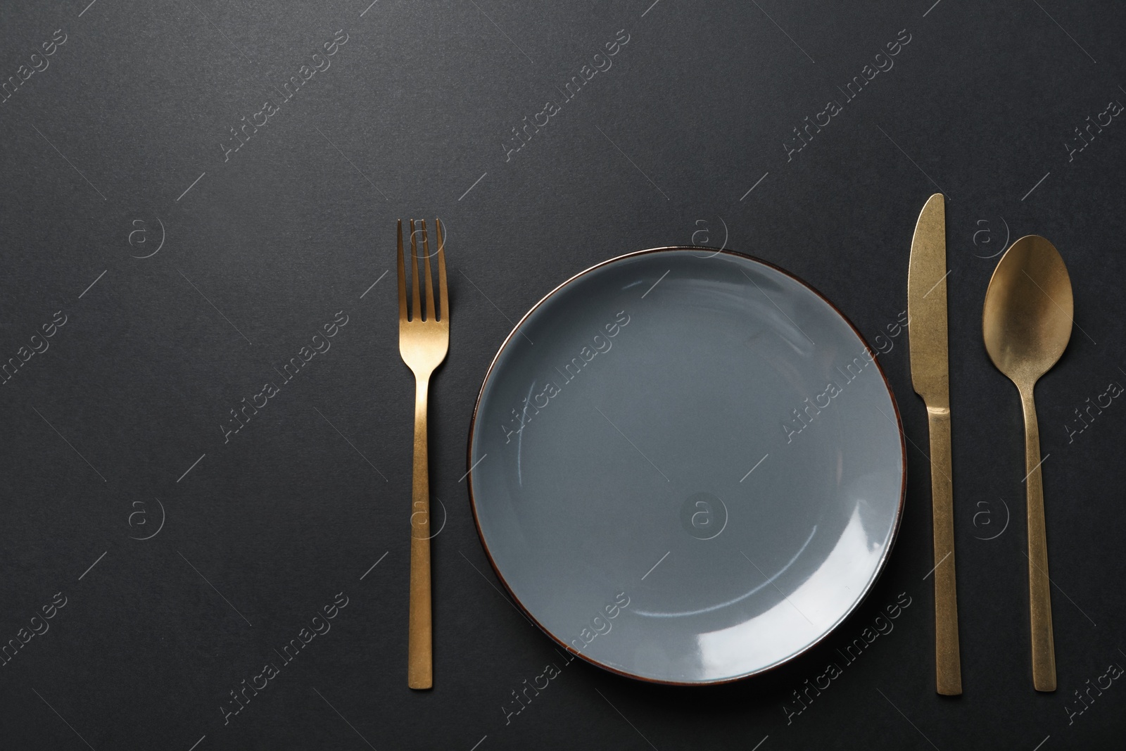 Photo of Elegant golden cutlery and plate on black background, flat lay. Space for text