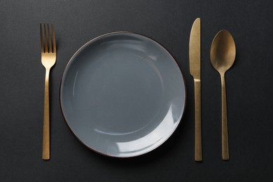 Photo of Elegant golden cutlery and plate on black background, flat lay