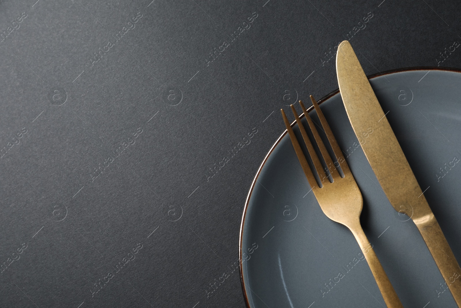 Photo of Elegant golden cutlery and plate on black background, top view. Space for text