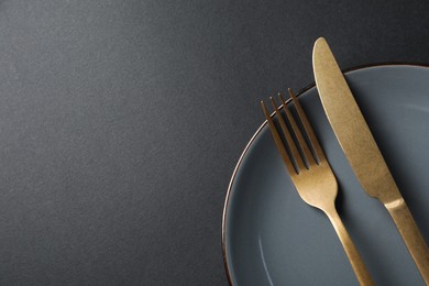 Elegant golden cutlery and plate on black background, top view. Space for text