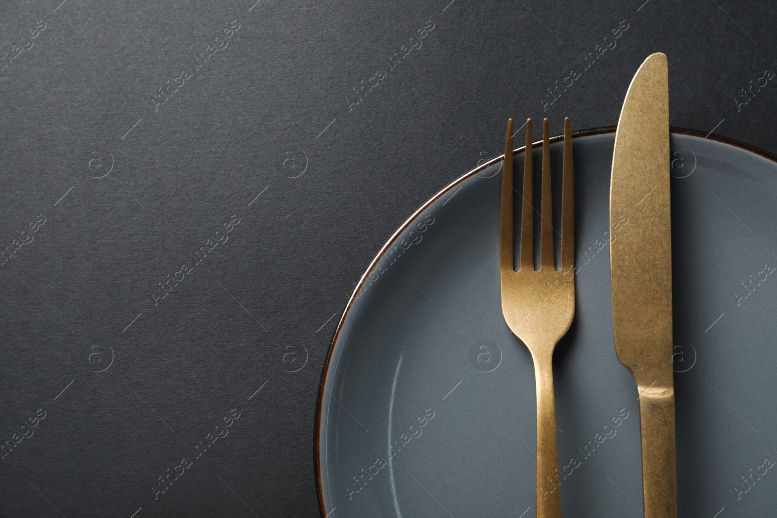 Photo of Elegant golden cutlery and plate on black background, top view. Space for text