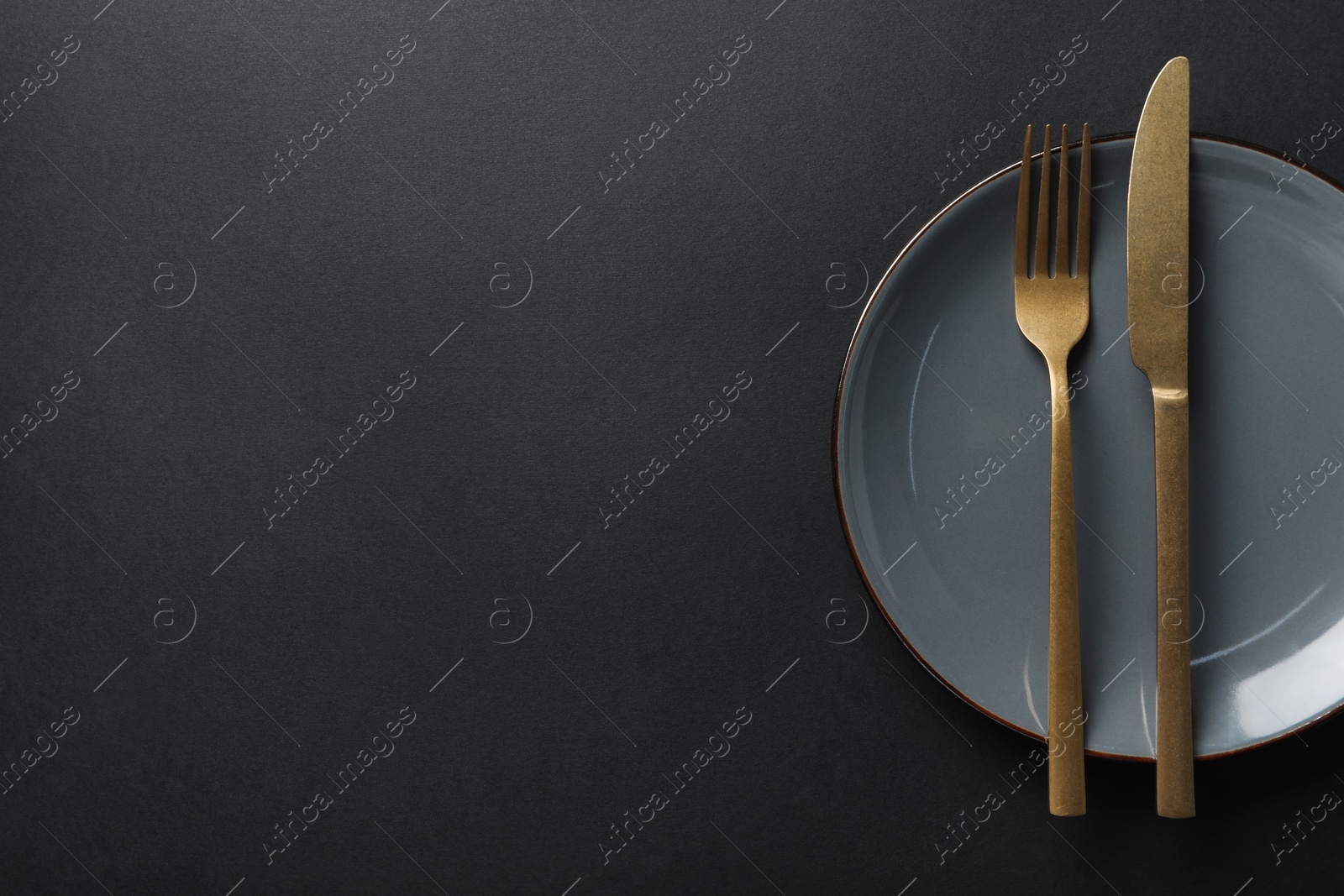 Photo of Elegant golden cutlery and plate on black background, top view. Space for text