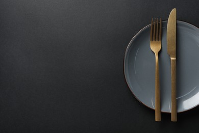 Photo of Elegant golden cutlery and plate on black background, top view. Space for text