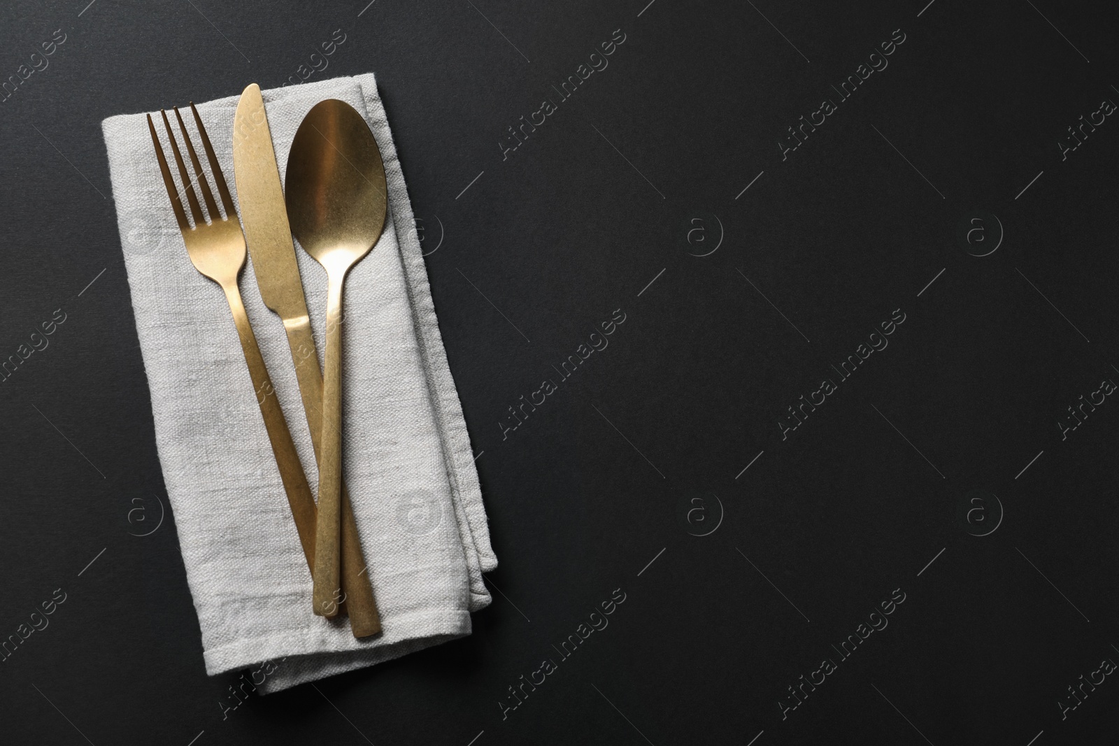 Photo of Elegant golden cutlery and napkin on black background, top view. Space for text