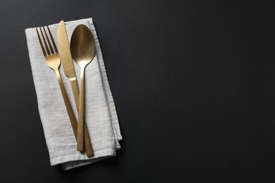 Elegant golden cutlery and napkin on black background, top view. Space for text