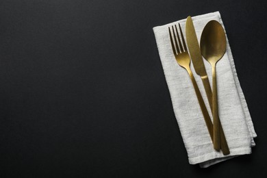 Photo of Elegant golden cutlery and napkin on black background, top view. Space for text