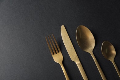 Photo of Elegant golden cutlery on black background, flat lay. Space for text