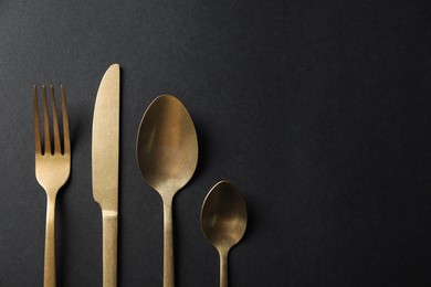 Photo of Elegant golden cutlery on black background, flat lay. Space for text