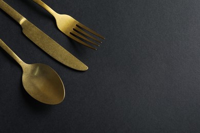 Photo of Elegant golden cutlery on black background, above view. Space for text