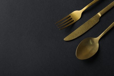 Photo of Elegant golden cutlery on black background, above view. Space for text