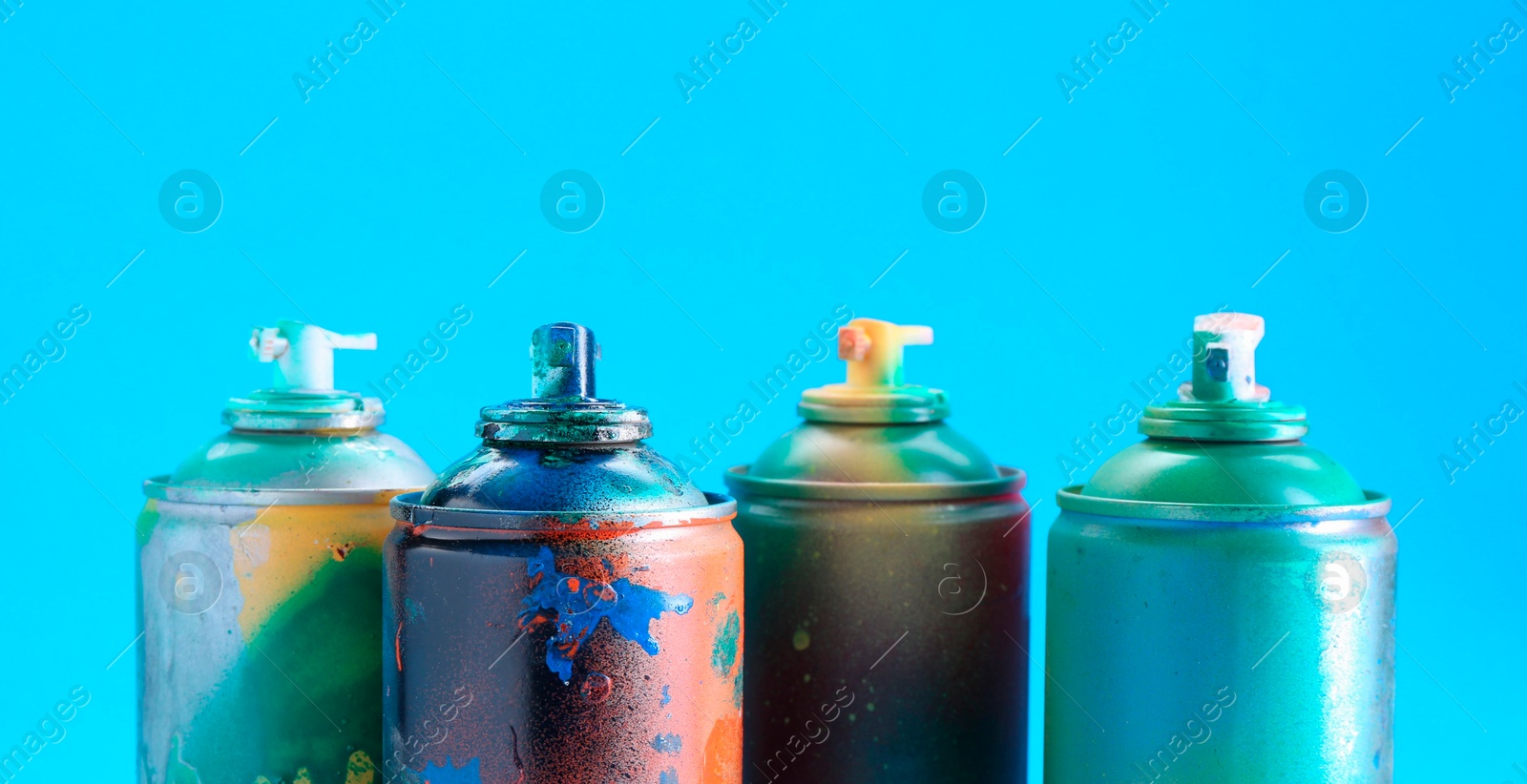 Photo of Many spray paint cans on light blue background, closeup