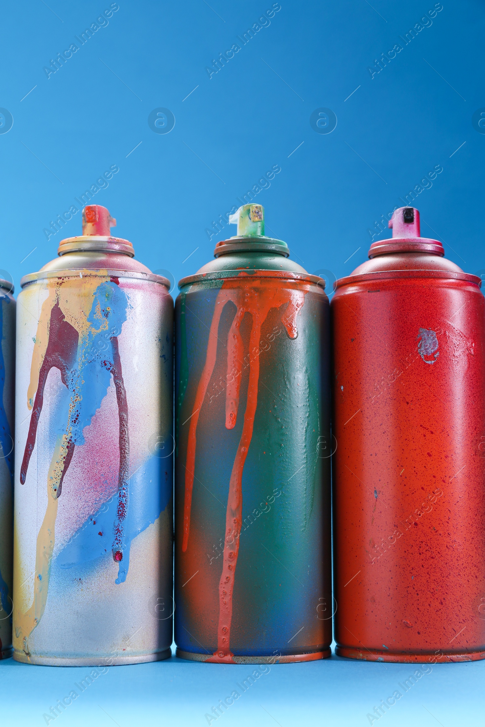 Photo of Many spray paint cans on light blue background, low angle view