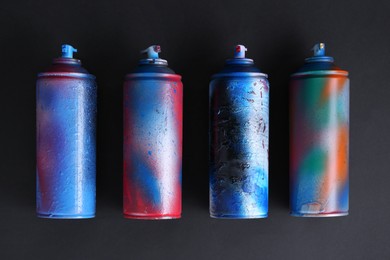 Photo of Many spray paint cans on dark background, flat lay