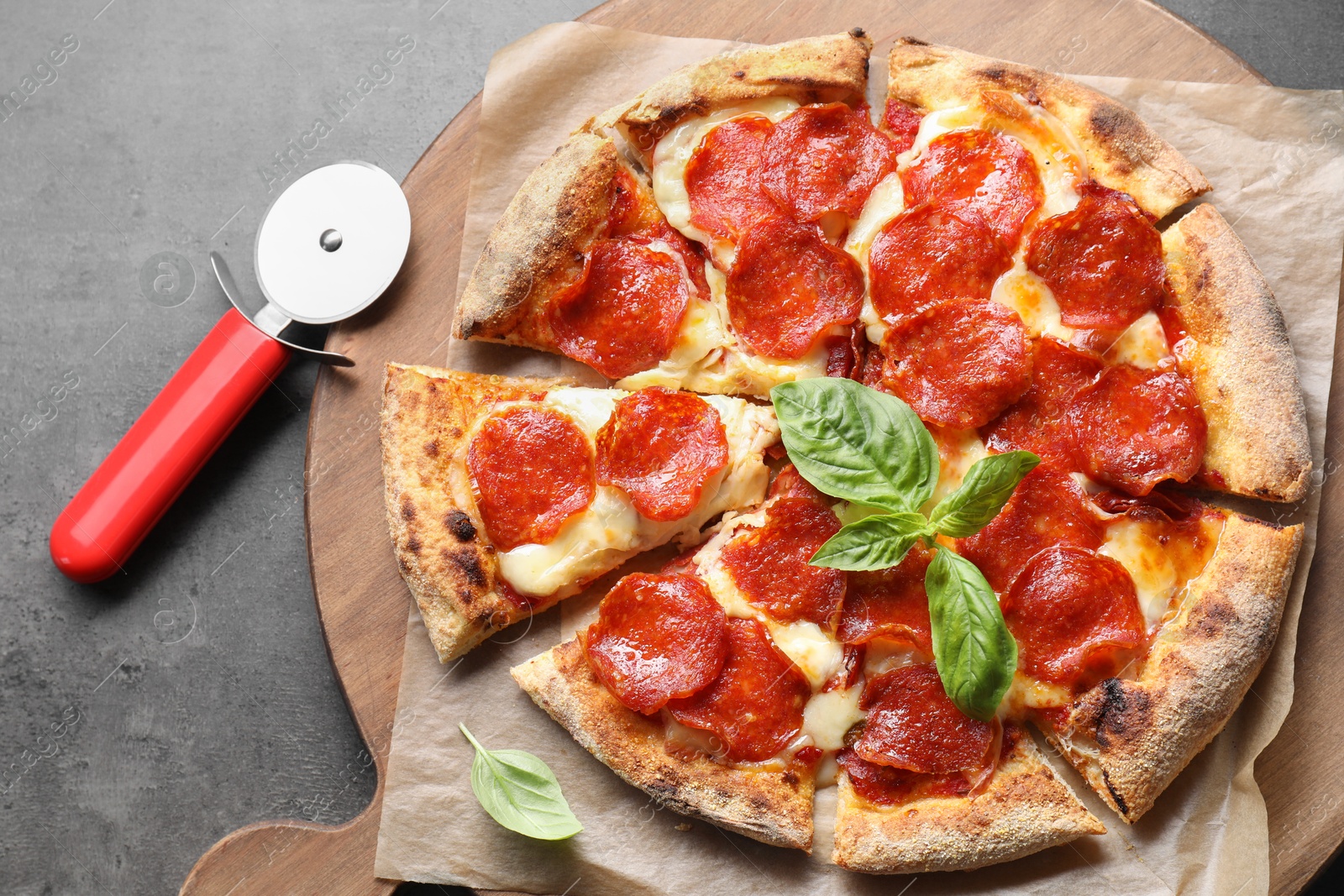 Photo of Tasty pepperoni pizza with basil and cutter on grey table, top view