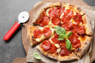 Tasty pepperoni pizza with basil and cutter on grey table, top view