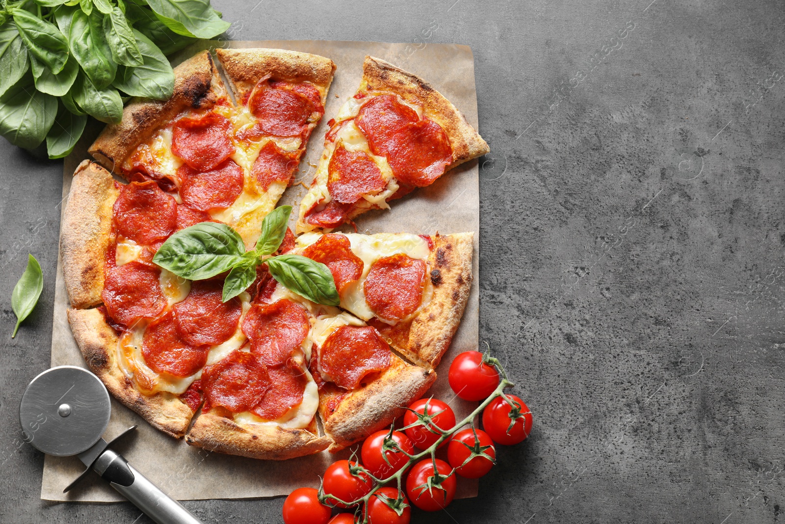 Photo of Tasty pepperoni pizza, cutter and ingredients on grey table, flat lay. Space for text