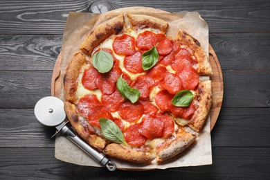 Tasty pepperoni pizza with basil and cutter on black wooden table, top view