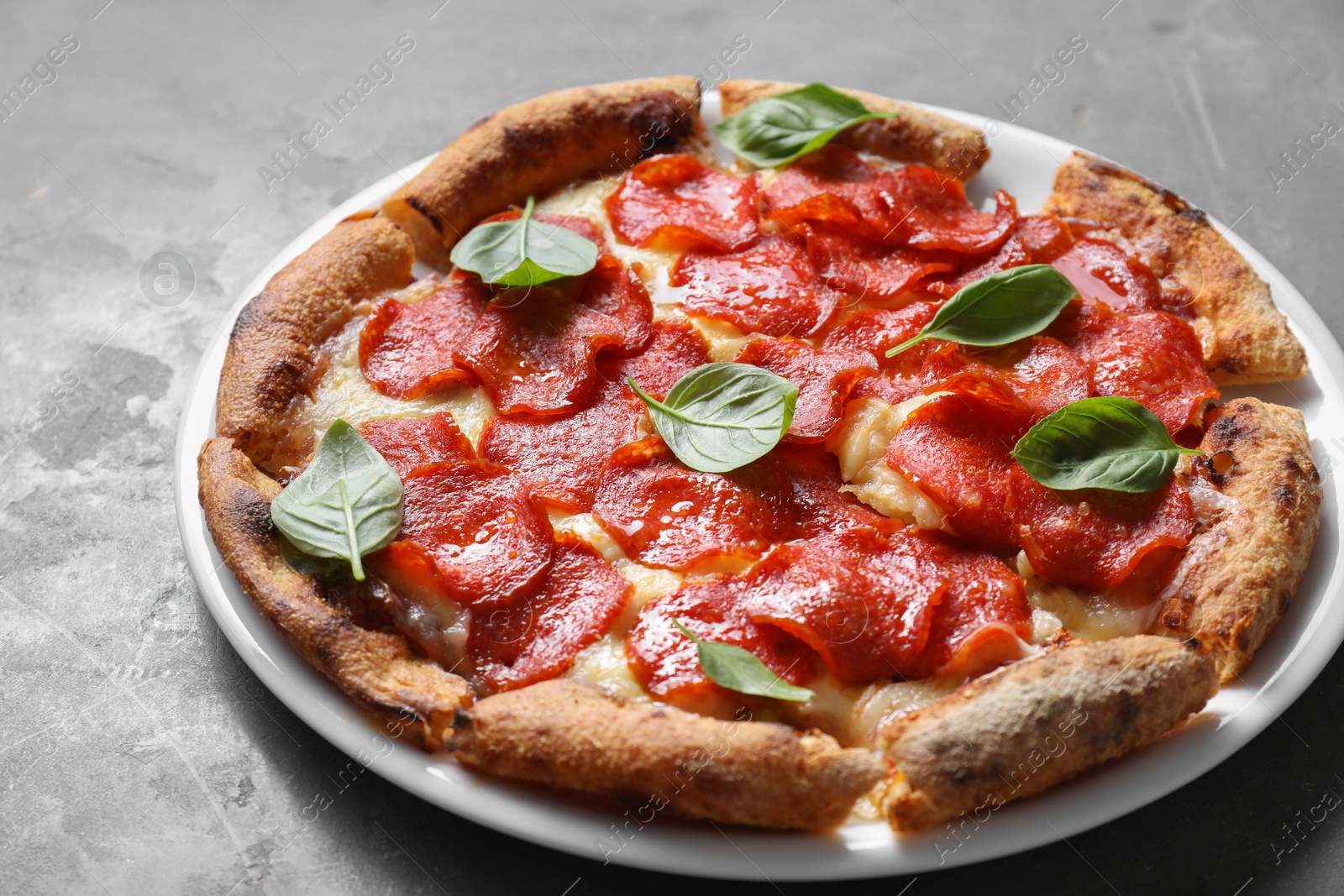 Photo of Tasty pepperoni pizza with basil on grey table