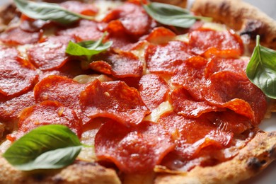 Tasty pepperoni pizza with basil on table, closeup