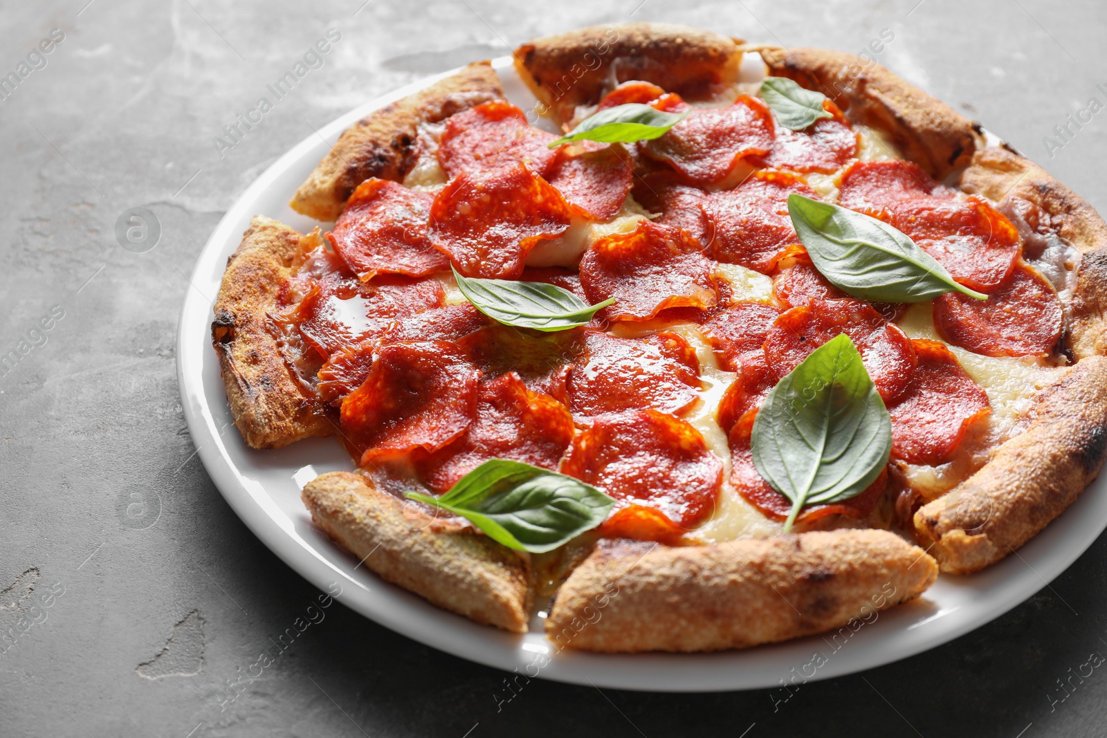 Photo of Tasty pepperoni pizza with basil on grey table