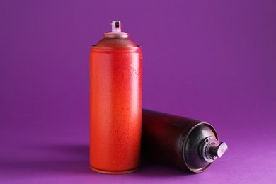 Photo of Two spray paint cans on violet background