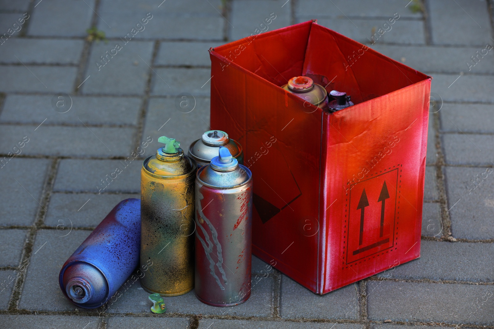 Photo of Many spray paint cans and red cardboard box outdoors