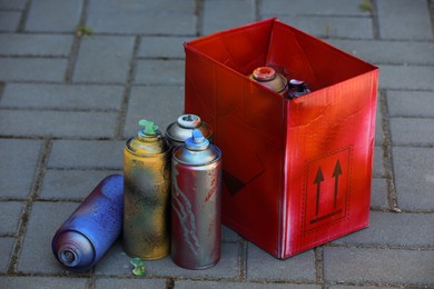 Many spray paint cans and red cardboard box outdoors