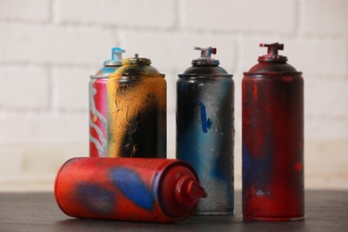 Many spray paint cans on gray surface against white brick wall